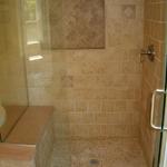 Custom tile shower with colored concrete seat, mosaic travertine floor and arched picture frame nook